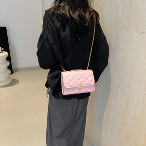 Pink quilted crossbody bag with gold chain strap shown on model in minimalist interior
