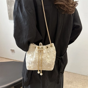 Chic woven beige bucket bag with delicate white floral patterns and gold chain strap