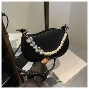 Détail d'un sac demi-lune noir avec breloques en cœur et décoration de bandoulière en perles