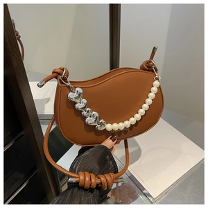 Détail d'un sac selle caramel avec chaîne cœur et perles sur fond décoratif en bois