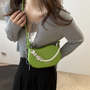 Sac demi-lune vert vif avec chaîne de perles et cœurs porté par un mannequin chic