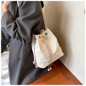 Detail of cream bucket bag with drawstring closure and pearl accents on the strap