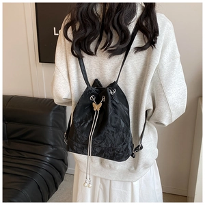Detail of black drawstring bucket backpack with gold butterfly buckle and pearl charms