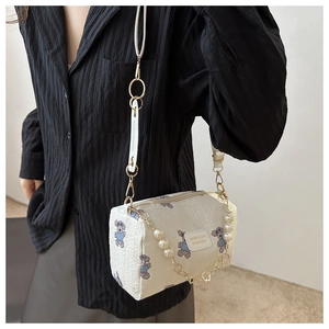 Détail du sac cylindre blanc avec motifs d'ours violets et chaîne en perles sur chemise