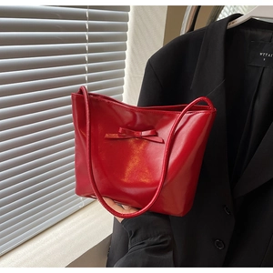 Detail of red patent leather tote bag with bow accent and slim shoulder straps