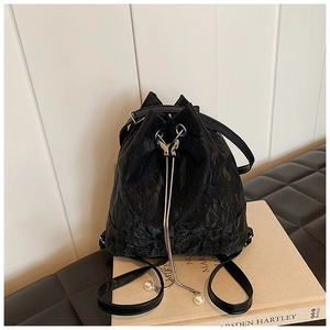 Detail of black drawstring bucket bag with butterfly metal clasp and pearl accents