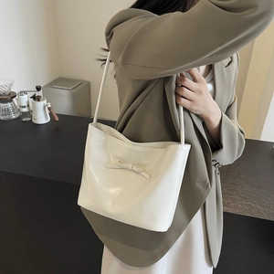 Cream white bucket bag with bow detail and glossy leather finish on model shoulder