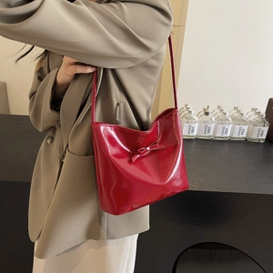Minimalist red patent leather underarm bucket bag with bow detail worn by model