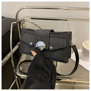 Détail du sac bandoulière noir avec rabats décoratifs et grand fermoir rond en métal