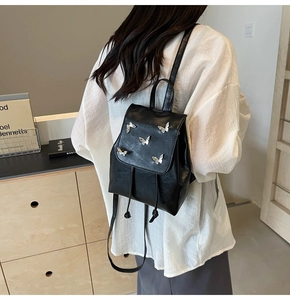 Detail of a black leather mini backpack with 3D silver butterfly charms on the flap