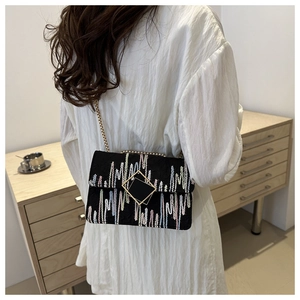 Detail of black crossbody bag featuring colorful geometric embroidery and gold buckle