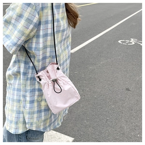 Detail of light pink drawstring bucket phone bag worn by a model in casual plaid shirt