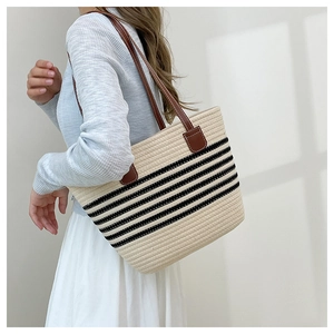 Detail of woven straw tote bag featuring brown leather straps and black horizontal stripes