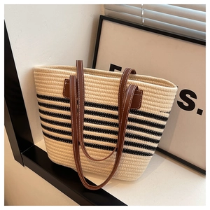 Detail of straw tote bag showing black stripes and brown leather strap with stitching