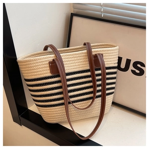 Close-up of woven tote bag with black stripes and brown leather straps featuring white stitching