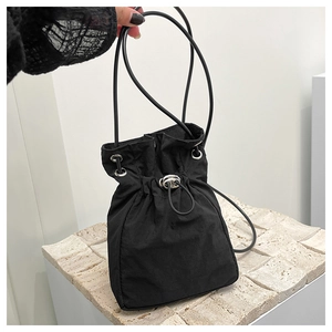 Detail of black nylon drawstring bucket bag with silver eyelets on a stone base
