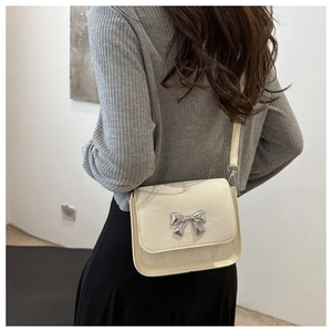 Detail of a creamy white crossbody bag with a silver bow accent on a model's waist