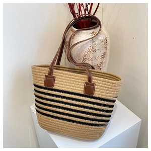 Detail of woven straw tote bag with black stripes and brown faux leather handle