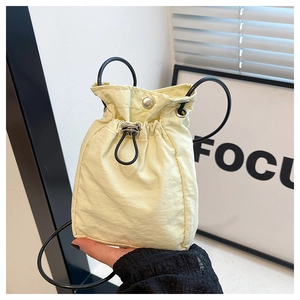 Detail of pale yellow drawstring crossbody bag with silver buckle and black handles