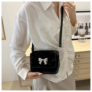 Detail of a black glossy crossbody bag with a silver metal bow accent and slim strap