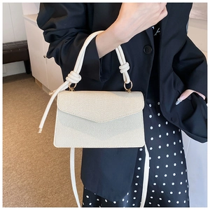 Detail of cream diagonal textured crossbody bag with thick rope handle and gold hardware