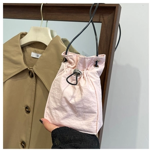 Detail of a light pink drawstring bucket bag with slim black strap and silver hardware