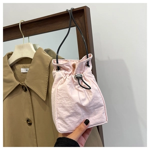Detail of a light pink drawstring bucket bag with black thin rope handles and nylon fabric