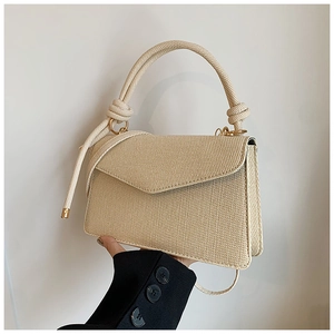 Detail of beige woven handbag with knot handle, gold rings, and accordion-fold side design