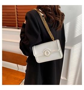 Model wearing a minimalist cream shoulder bag with golden chain strap and round buckle detail