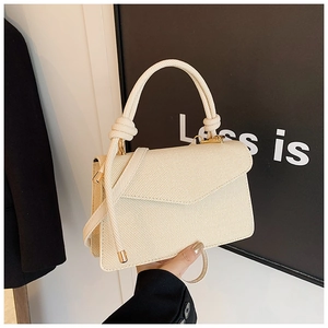 Detail of beige textured fabric shoulder bag with unique knotted handle and gold metal hardware