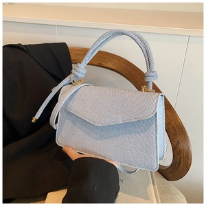 Detail of light blue twill fabric handbag with knot handle on a wooden chair