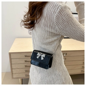Détail d'un mini sac en cuir verni noir avec un nœud argenté et une bandoulière chaîne
