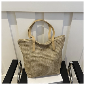 Dettaglio della borsa tote in paglia intrecciata con manici in pelle e chiusura a zip