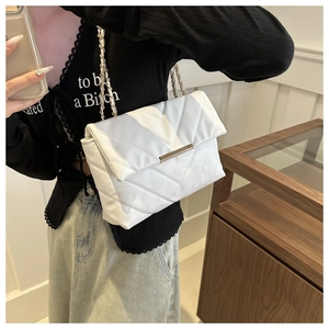 Detailed view of white quilted crossbody bag with gold buckle and chain strap on model