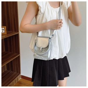 Détail d'un sac bandoulière argenté avec texture plissée et boucle en métal sur modèle