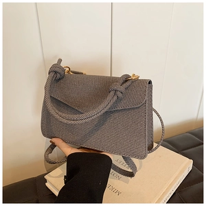 Detail of grey twill fabric handbag featuring a unique knotted handle and gold metal hardware