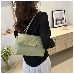 Green V-quilted crossbody bag with gold metal chain strap worn by a model in a room