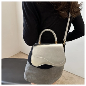 Detail view of silver metallic bag featuring a unique asymmetrical flap and braided handle