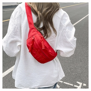 Detail of red crossbody bag showing embroidered text and woven zipper pulls on white shirt