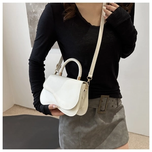 Detail of white crossbody bag with unique wavy flap design and woven top handle
