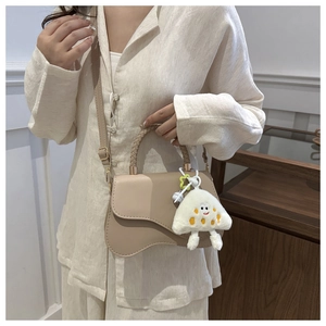 Detail view of beige crossbody bag with woven handle and plush charm accessory