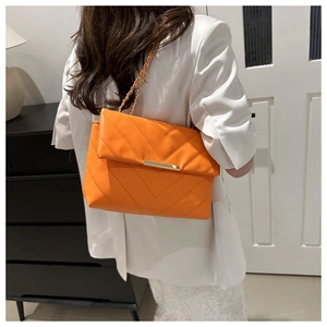 Detail of orange quilted crossbody bag featuring V-shaped stitching and gold metal clasp