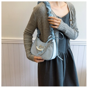 Detail of light blue pleated shoulder bag featuring silver bow, chain and pearl strap