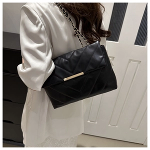 Detail of black quilted chain shoulder bag with V-shaped pattern and gold metal hardware