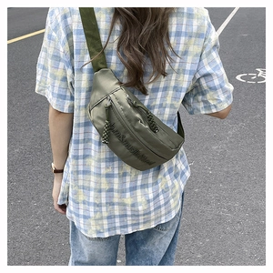 Outdoor back view of an olive green nylon sling bag with adjustable strap and dual zippers