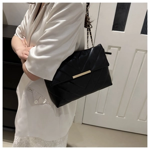 Detail of black quilted leather shoulder bag with gold chain strap and metal lock closure