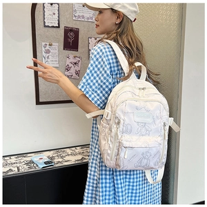 Side view of beige backpack with bear patterns on student in checkered dress