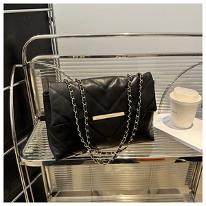 Detail of black quilted shoulder bag with V-shaped stitching and golden metal chain strap