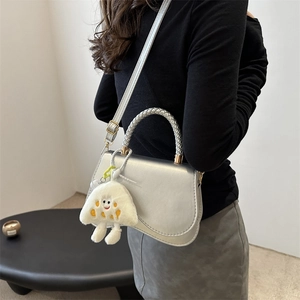 Silver metallic crossbody bag with white woven handle and plush charm on a model