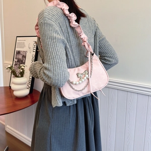 Pink velvet underarm bag with bow, pearl chain and ruffled strap shown on model shoulder